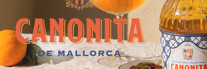 Canonita de Mallorca Sommer Aperitif auf Orangenbasis steht auf einem Tisch mit mediterranen Essen und frischen Früchten. 
