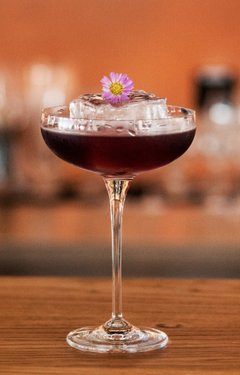 Ein Glas gefüllt mit einer roten Spirituose steht auf dem Tresen einer Bar 