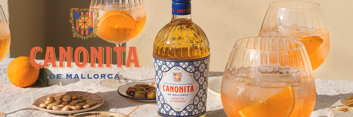 Canonita de Mallorca Sommer Aperitif auf Orangenbasis steht auf einem Tisch mit mediterranen Essen und frischen Früchten. 