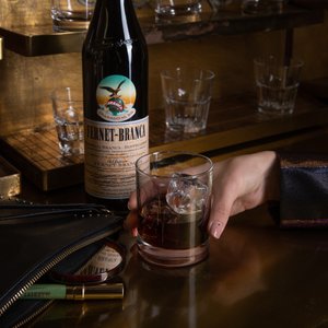  Hand mit Cocktailglas und Fernet-Branca Flasche