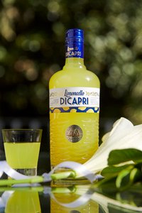 Eine schöne gelbfarbene Limoncello DICAPRI Flasche steht neben einem gefüllten Shotglas auf einem Tisch