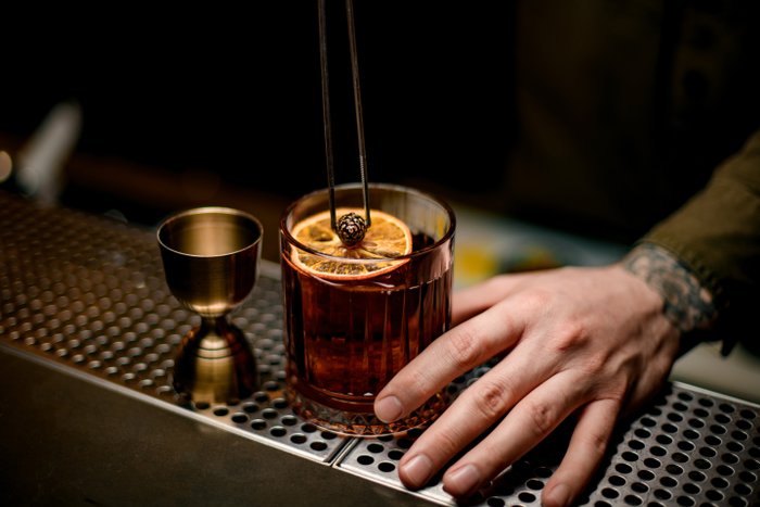 Ein Cocktail wird an der Bar zubereitet, die Hand des Barkeepers stellt das Glas gerade auf die Theke