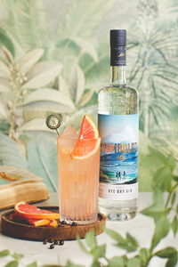 Flasche Humboldt Gin neben einem Glas, das mit einem Blutorangencocktail aus Humboldt Gin gefüllt ist. Das Bild zeigt die Flasche und das Getränk in stilvoller Präsentation, das den Gin und seine Verwendung in Cocktails hervorhebt.