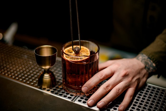 Ein Cocktail wird an der Bar zubereitet, die Hand des Barkeepers stellt das Glas gerade auf die Theke