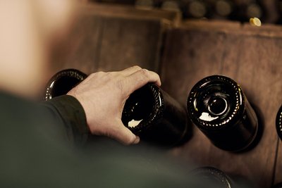 Eine Hand greift nach einer Geldermann Sektflasche, die gerade noch umgekehrt im Sektregal im Weinkeller liegt.