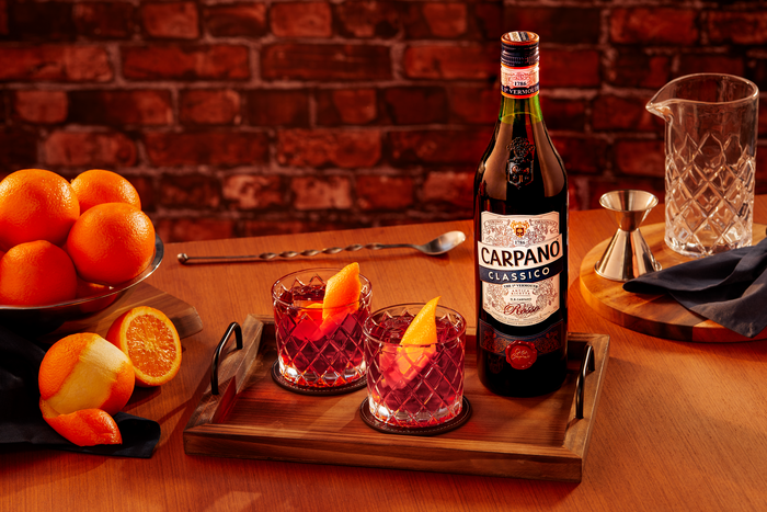 Carpano Classico Flasche auf einem Tisch mit zwei Gläsern Negroni und Orangen als Deko