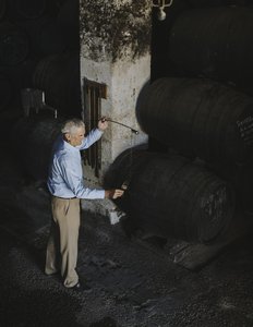 Ein Kellermeister steht im Weinkeller und füllt Carlos Brandy in ein Glas.
